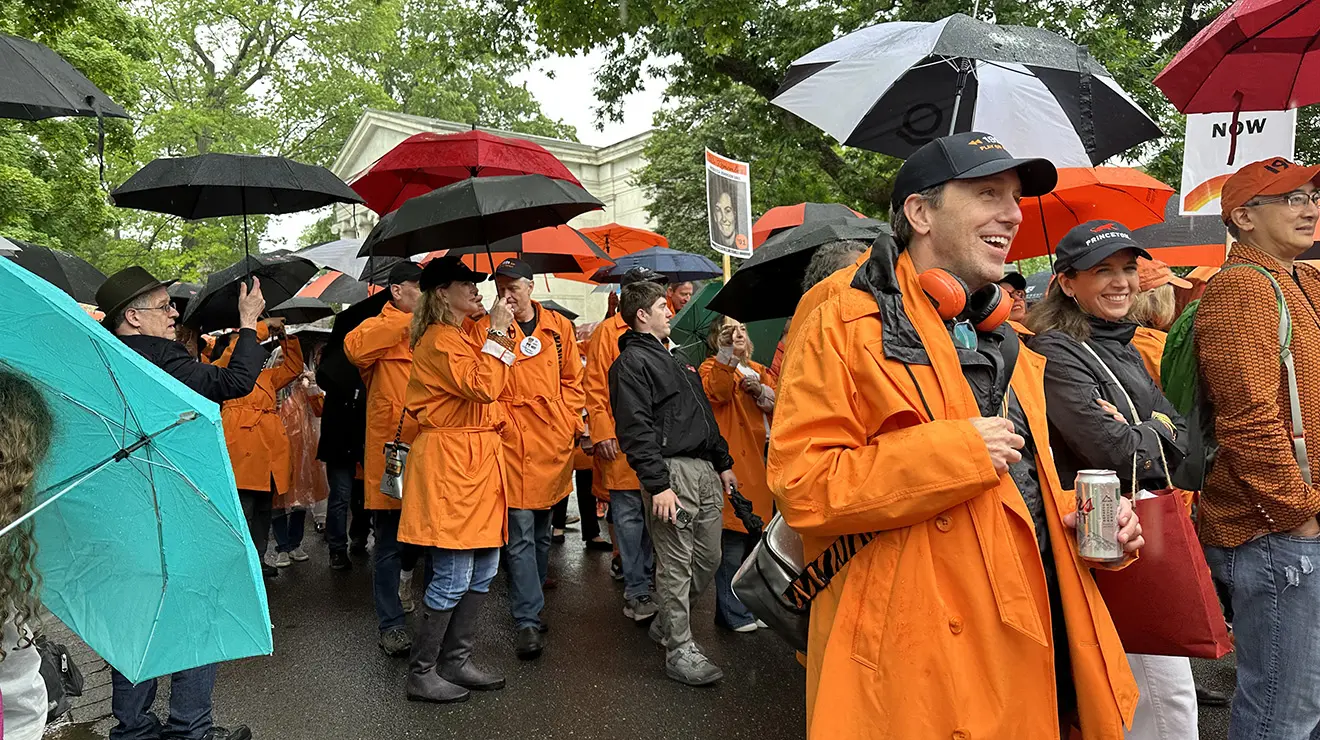 JulieReunions1_cropped_0.jpg People wearing orange rain jackets hold umbrellas and march in the 2026 P-rade.