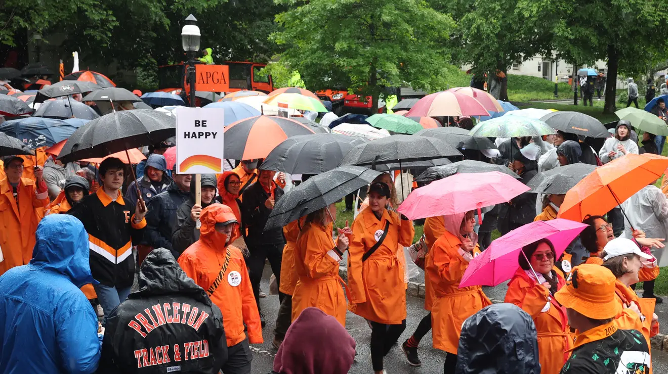 PRADE_Be Happy_Bev.jpg A crowd of people wearing orange and carrying umbrellas; someone holds up a sign with a rainbow and the words "be happy."