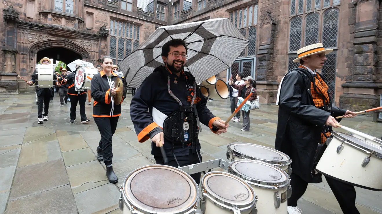 PRADE_Funky Drummer_Kevin Birch.jpg A man plays four drums in a marching band going through the East Pyne building.