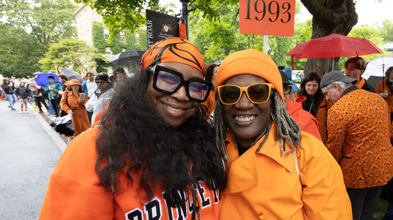 PRADE_Two women having fun_Kevin Birch.jpg Two women wear orange clothes in front of a sign reading 1993.